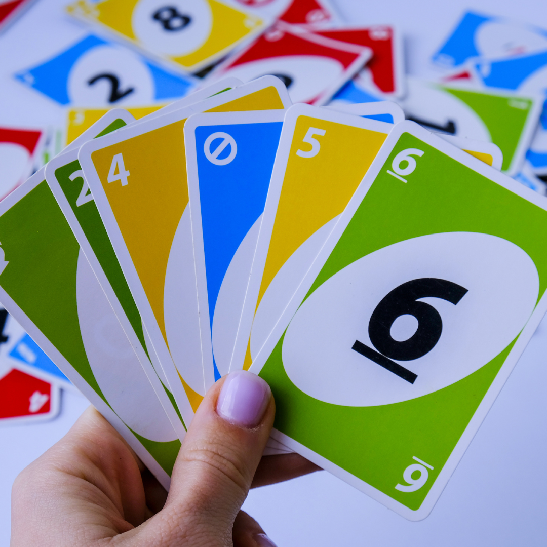 Image shows a hand holding Uno cards above a table with more Uno cards on it