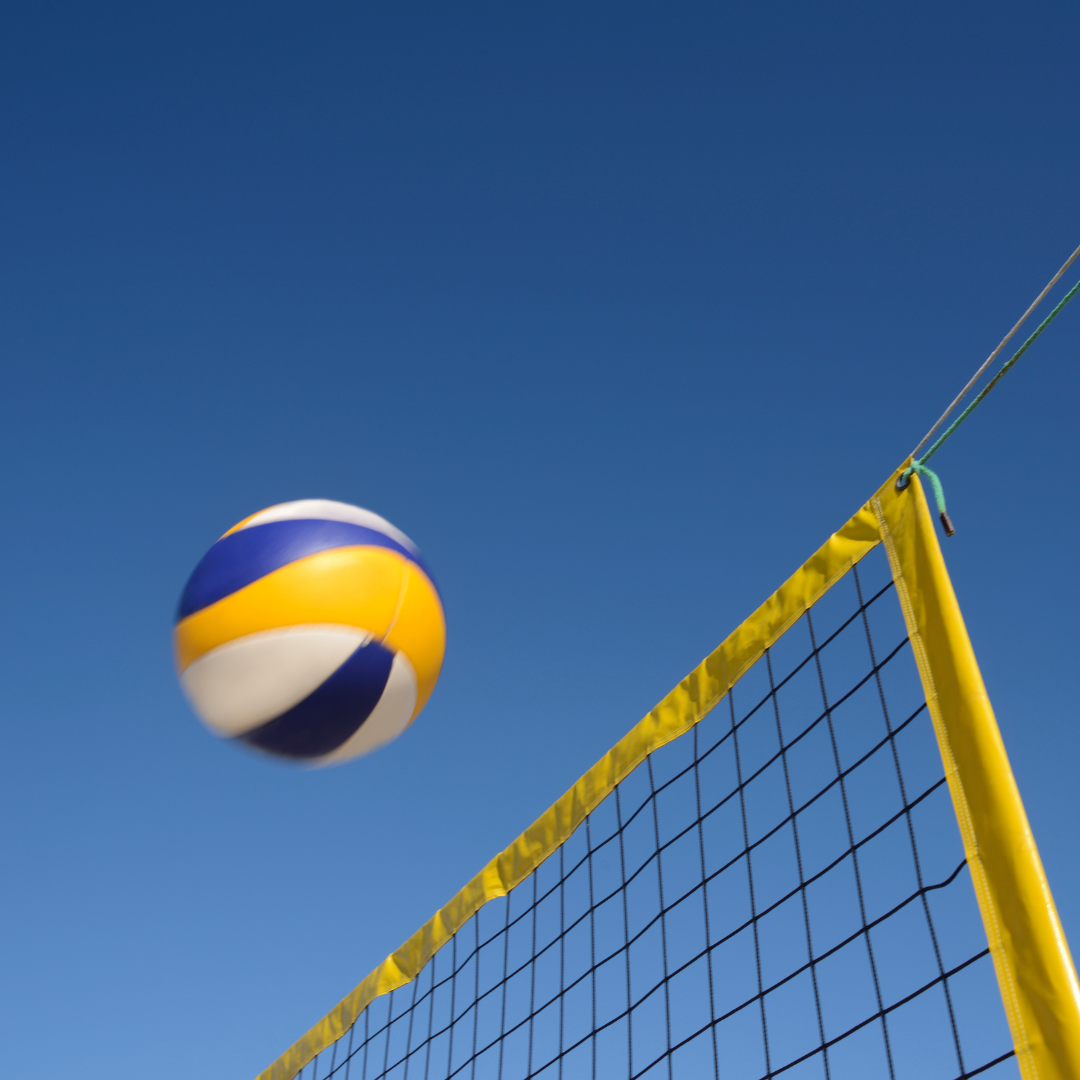 Image sdhows a volleyball and net aginst a blue sky.