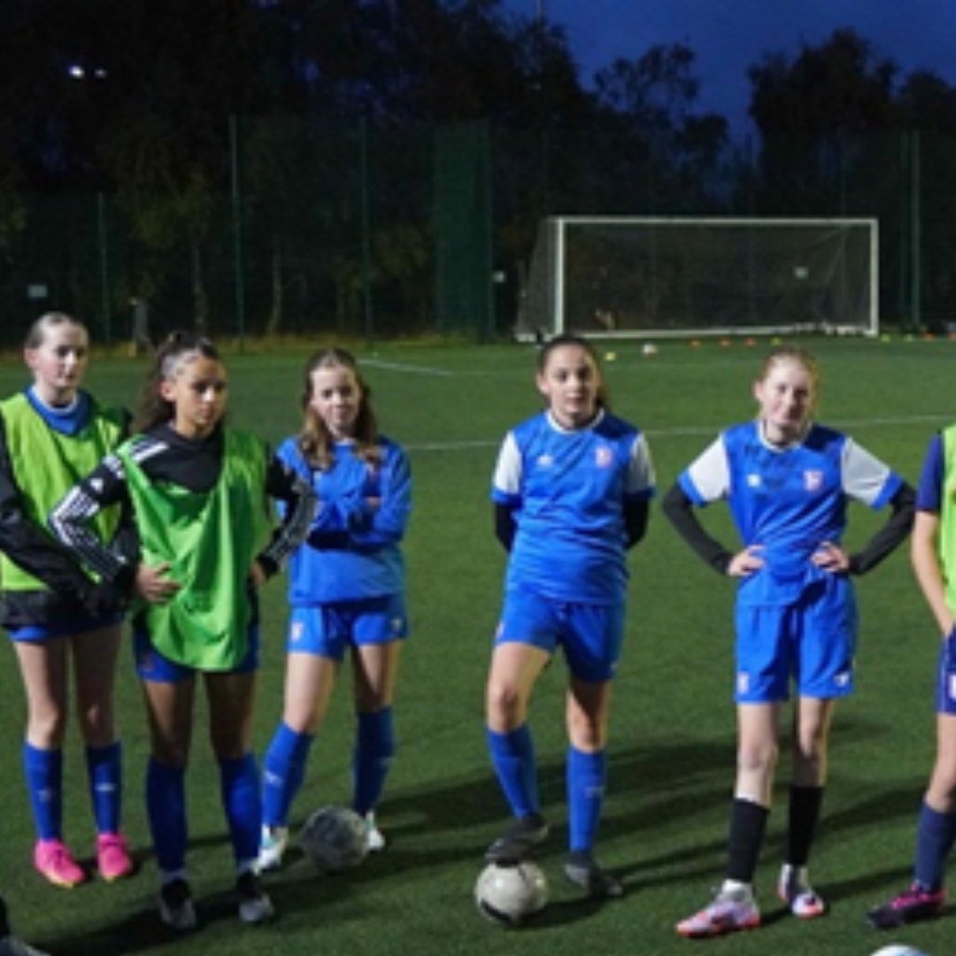 Image shows a group of girls gathered at the end of a football practice in the evening