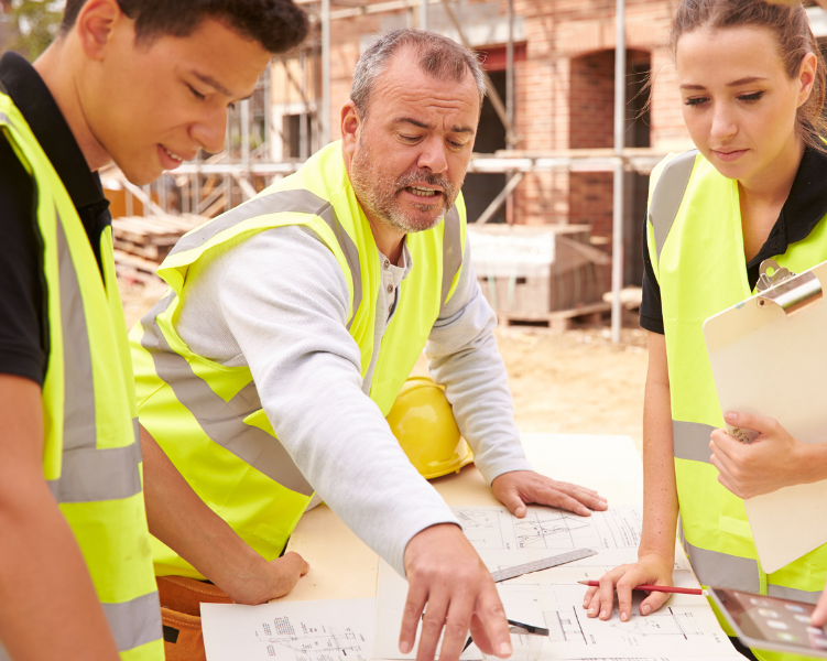 Construction workers wearing high-visibility vests reviewing building plans together at a construction site