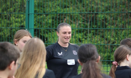 Cricket coach from Hampshire Cricket Board speaks to a group of pupils on the school field during a KS3 taster session.