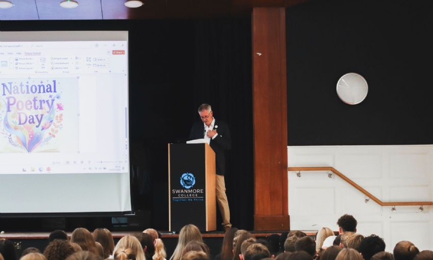 A speaker at a Swanmore College assembly, with a National Poetry Day graphic on screen and pupils seated in the school hall.