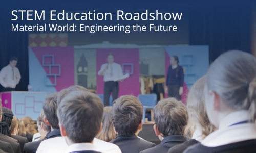 A shot taken from behind seated students watching two performers on stage during "The Material World" STEM roadshow.