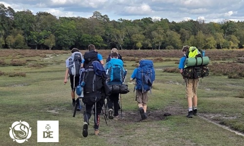 A group of students wearing large rucksacks hiking along a path through countryside terrain during a Duke of Edinburgh's Award expedition