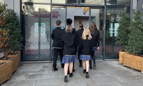A shot of the Swanmore College debate team students walking together toward the glass entrance of PGS